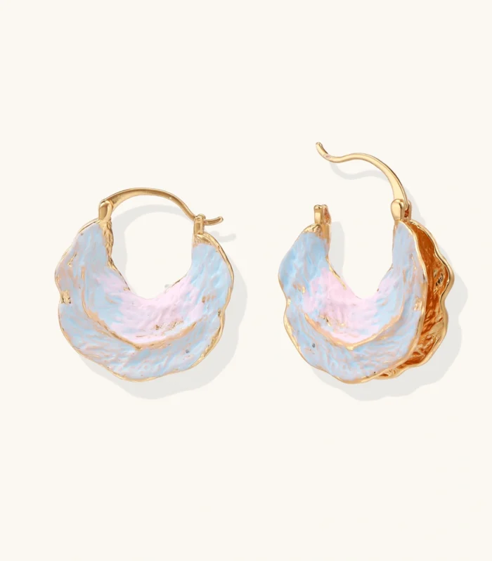 Shell-shaped hoop earrings with iridescent blue-pink enamel and gold trim on cream background