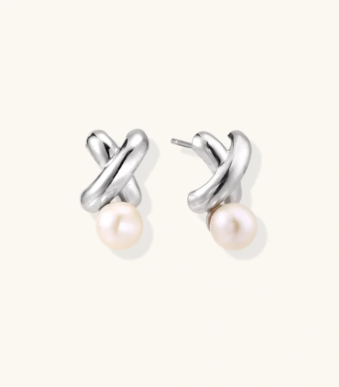 Rhodium-plated silver earrings with twisted X design and freshwater pearl drops on beige background