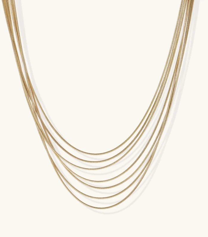 Seven delicate gold-plated snake chains create an elegant layered necklace on a neutral background.
