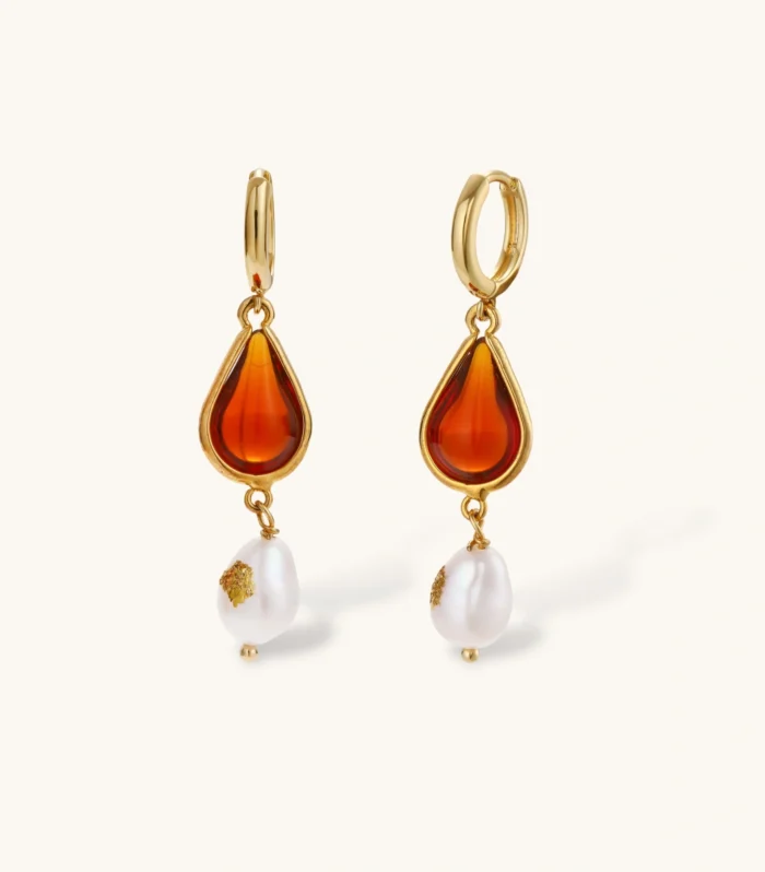 Gold-plated drop earrings featuring amber teardrops and white baroque pearls on light background.